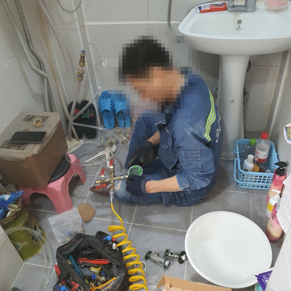욕실 바닥에 앉아 압력 게이지가 달린 밸브를 점검하는 모습